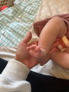 Postpartum doula Alexia gently holding a newborn baby’s foot during a home visit